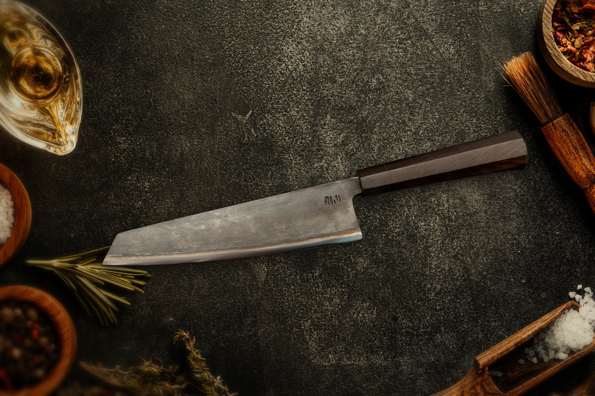 Couteau Chef Kiritsuke Forge Tay, finition carbone noir, sur ardoise avec épices et herbes