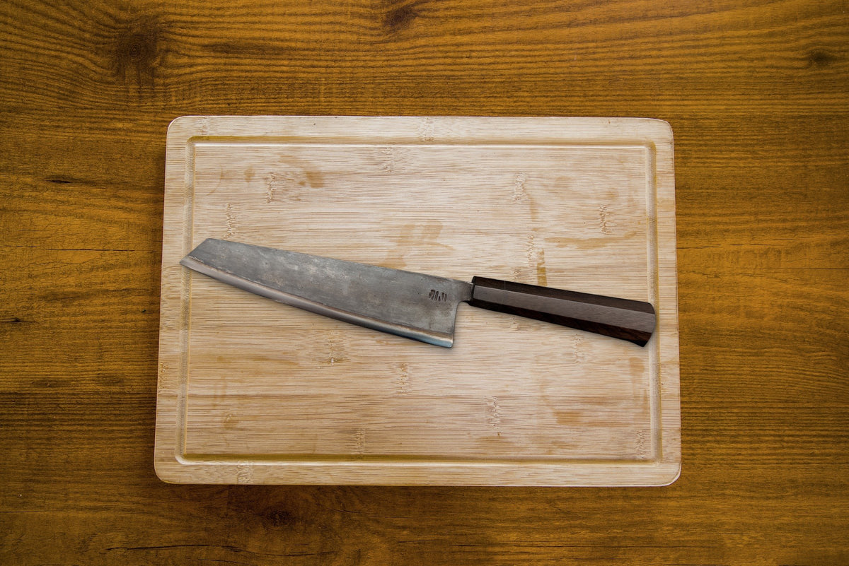 Couteau Chef Kiritsuke Forge Tay, finition carbone noir, sur planche en bois